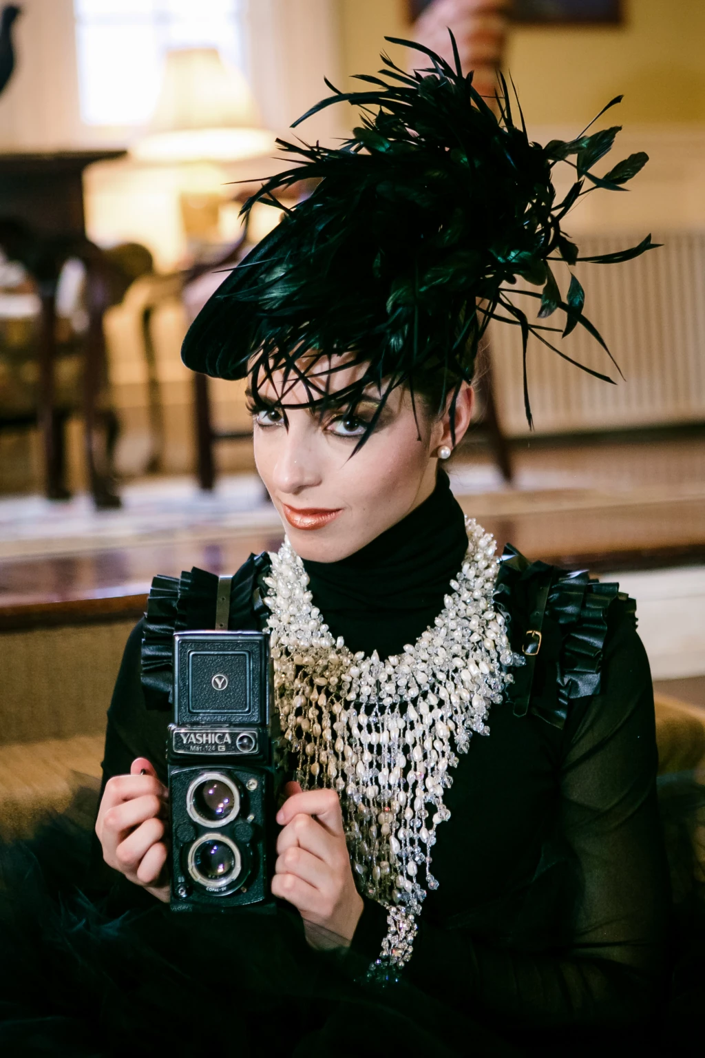 Editorial portrait of a woman in a feathered hat holding a vintage camera