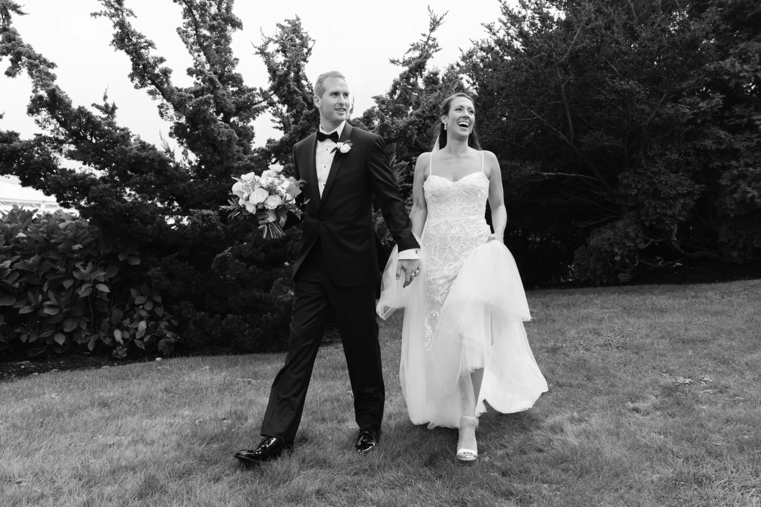 Black-and-white photo of a bride and groom walking across a lawn