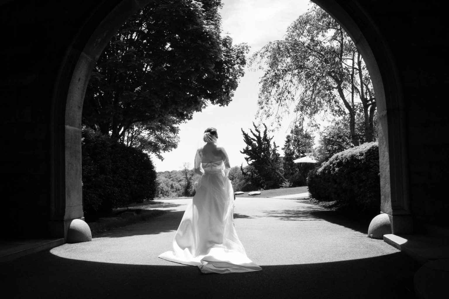 Black-and-white photo of a bride walking through a stone archway