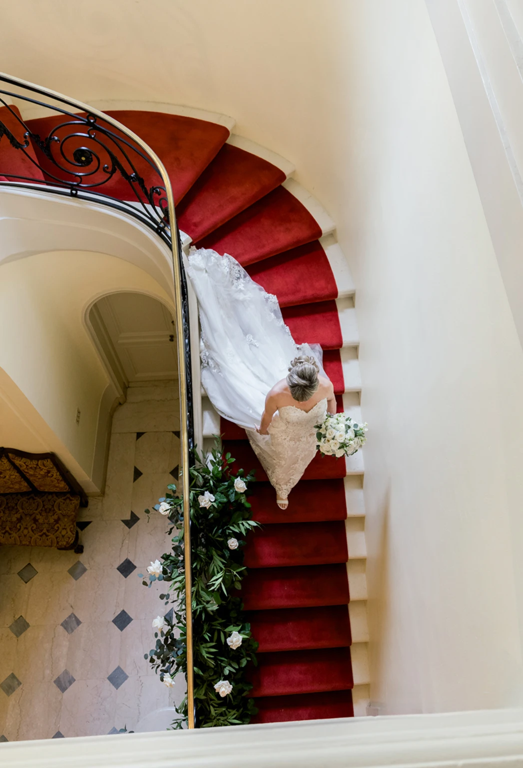 Bride descending a red-carpeted spiral staircase, seen from above