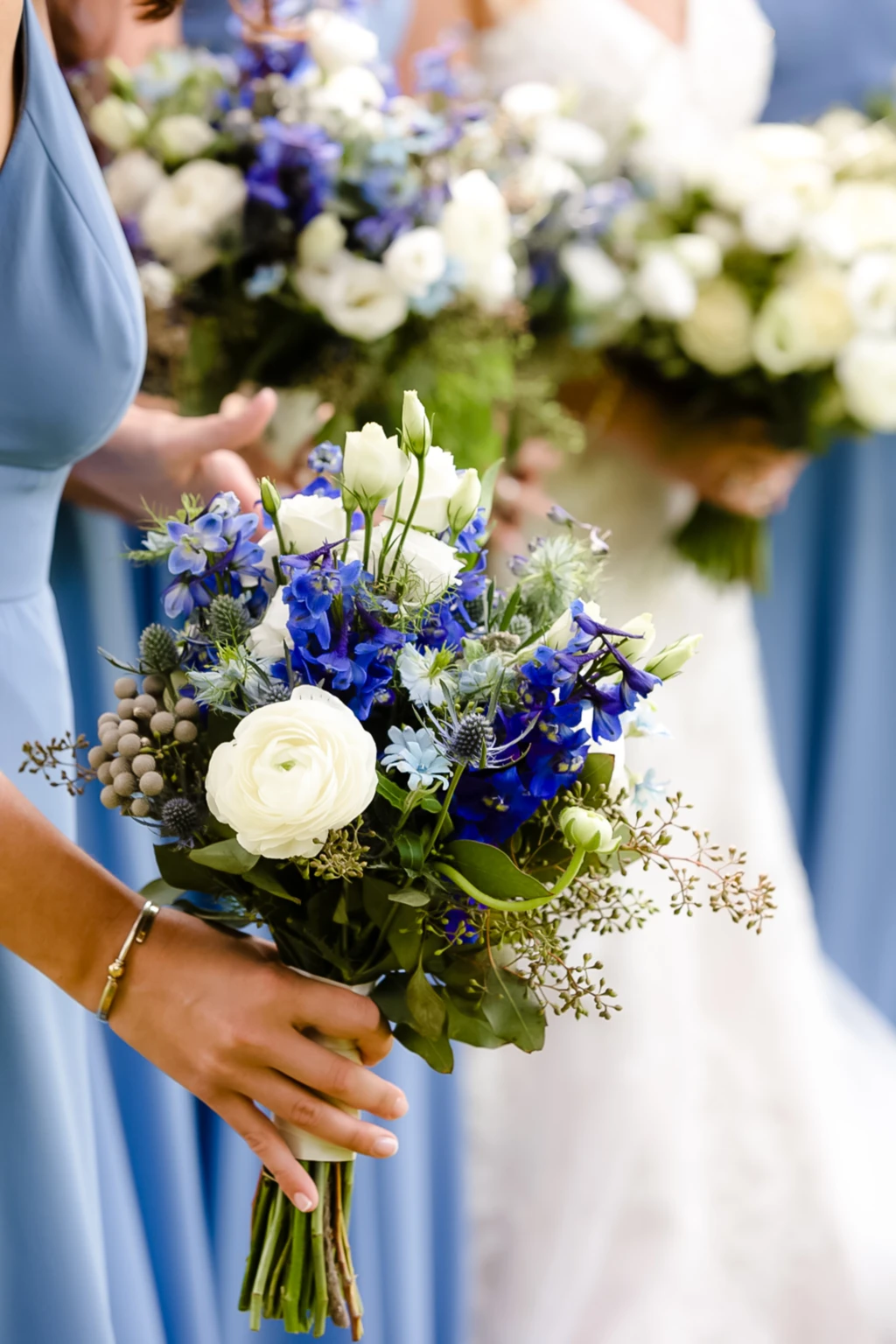 Bridesmaids in blue holding bouquets of blue and white flowers
