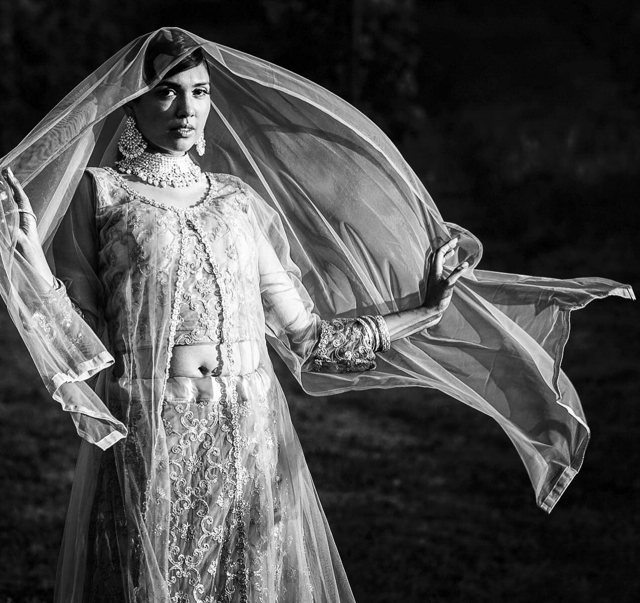 Bride in an embroidered lehenga with her veil flowing, in black and white