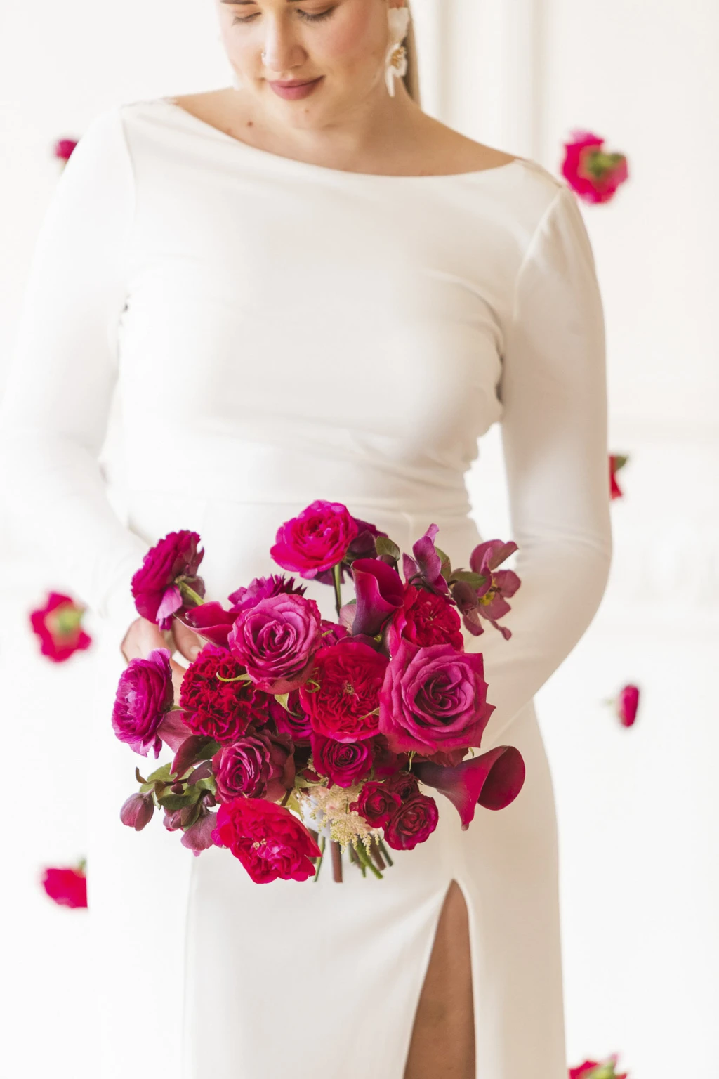 Bride in a long-sleeve gown holding a bouquet of red and pink ranunculus