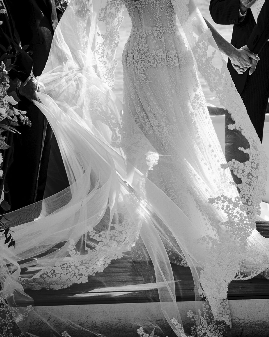 Black-and-white detail of a lace wedding gown and veil in motion