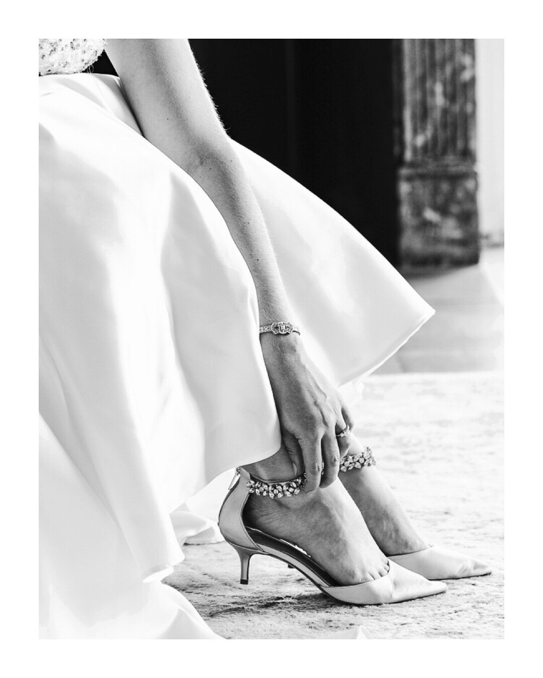 Black-and-white detail of a bride fastening her shoe