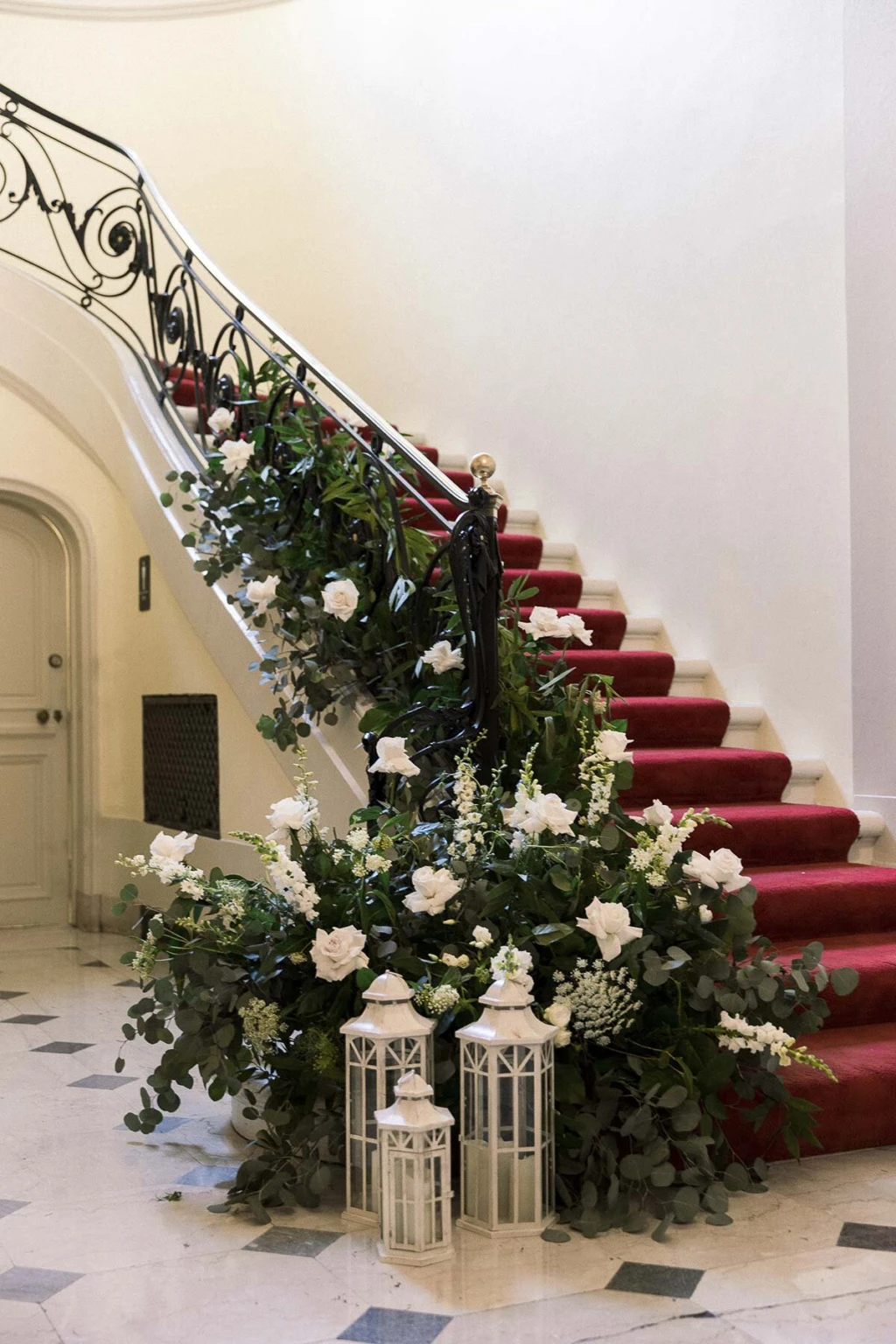 Red-carpeted staircase decorated with white flowers and lanterns