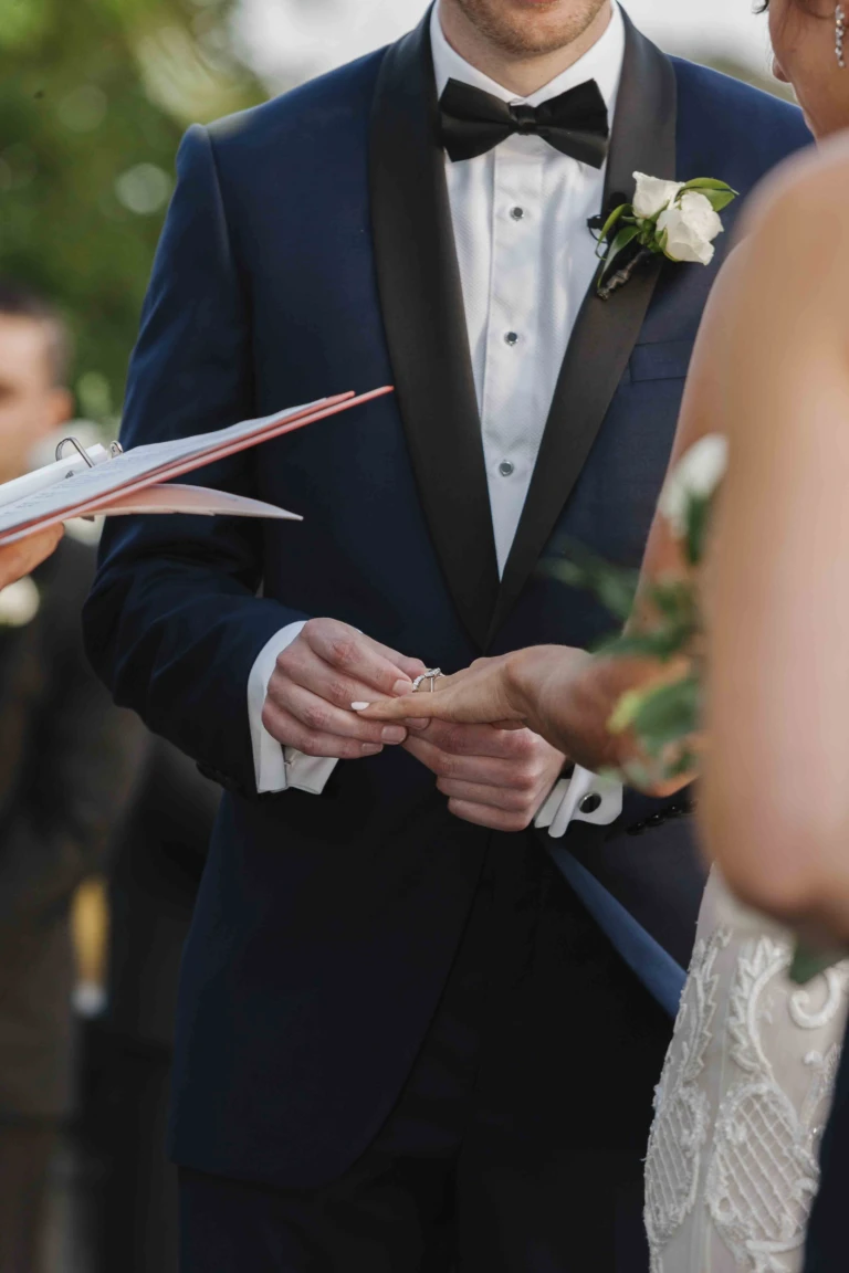 Groom in a navy tuxedo reading his vows