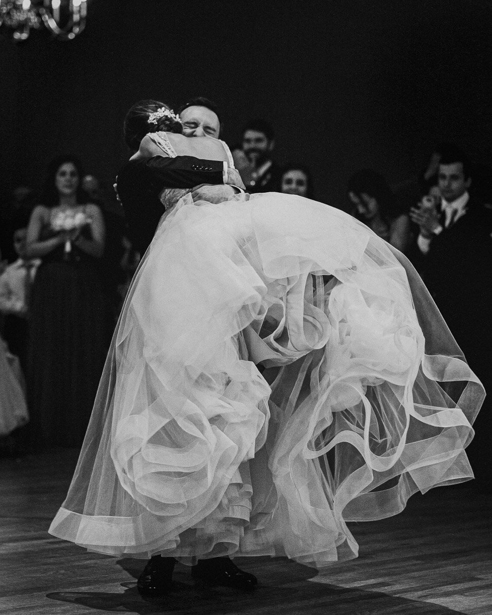 Groom lifting his bride in a tulle gown on the dance floor, in black and white
