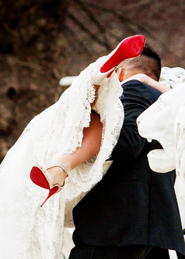 Groom carrying his bride, her red-soled heels in the air