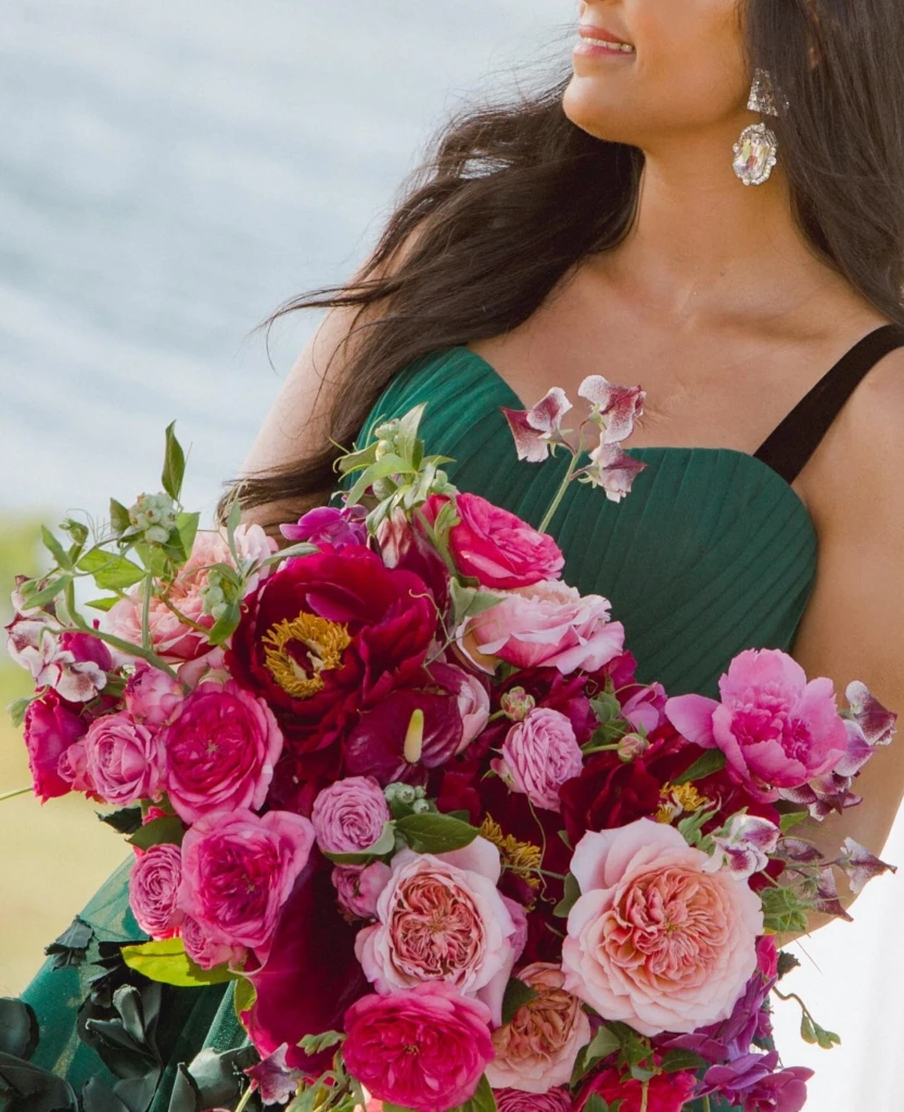 Bridesmaid in emerald green holding a bouquet of pink peonies and garden roses